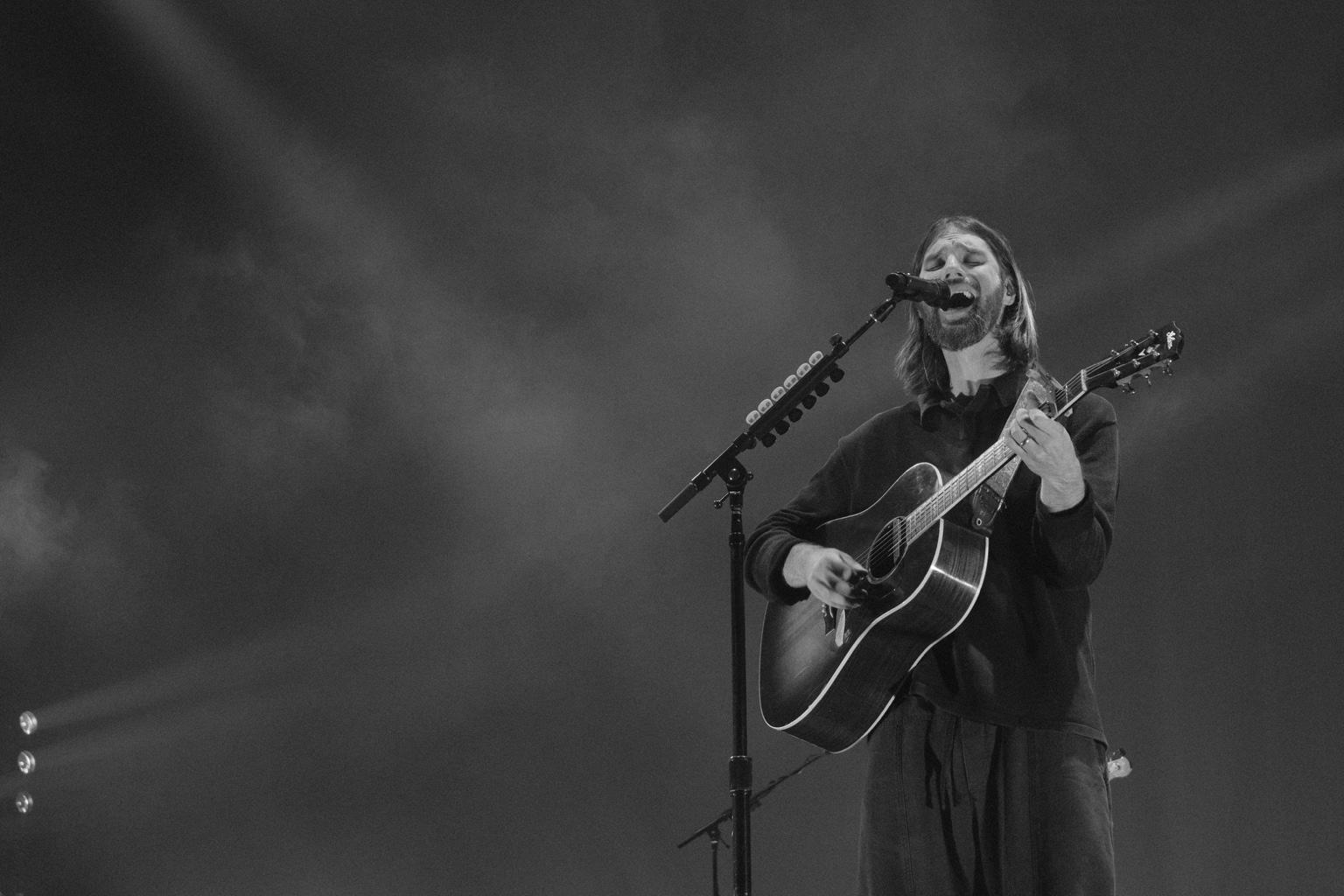 A vocalist sings into a microphone while playing acoustic guitar