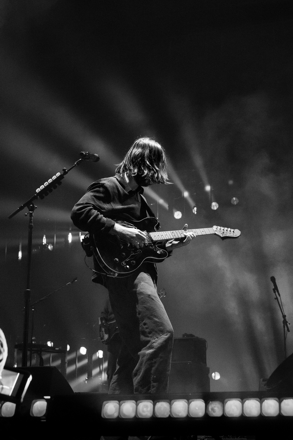 A guitarist turns toward the stage lights while playing electric guitar