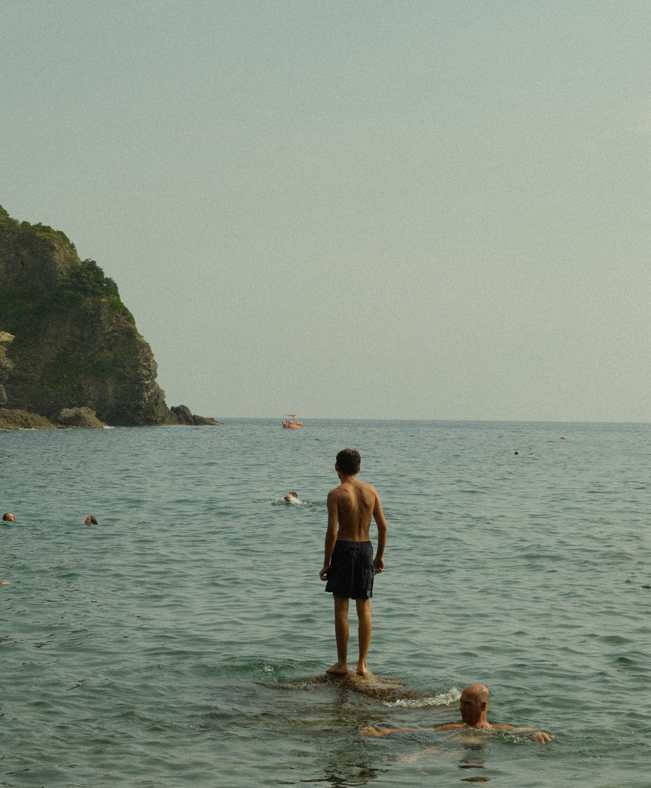 A swimmer stands on a rock in calm coastal water