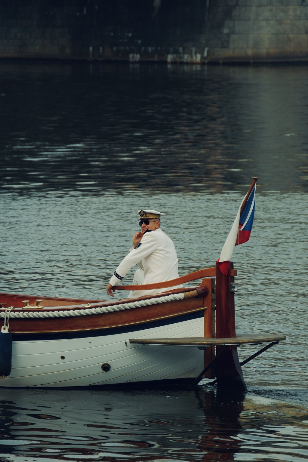 A person in a white shirt sits aboard a wooden boat on still water