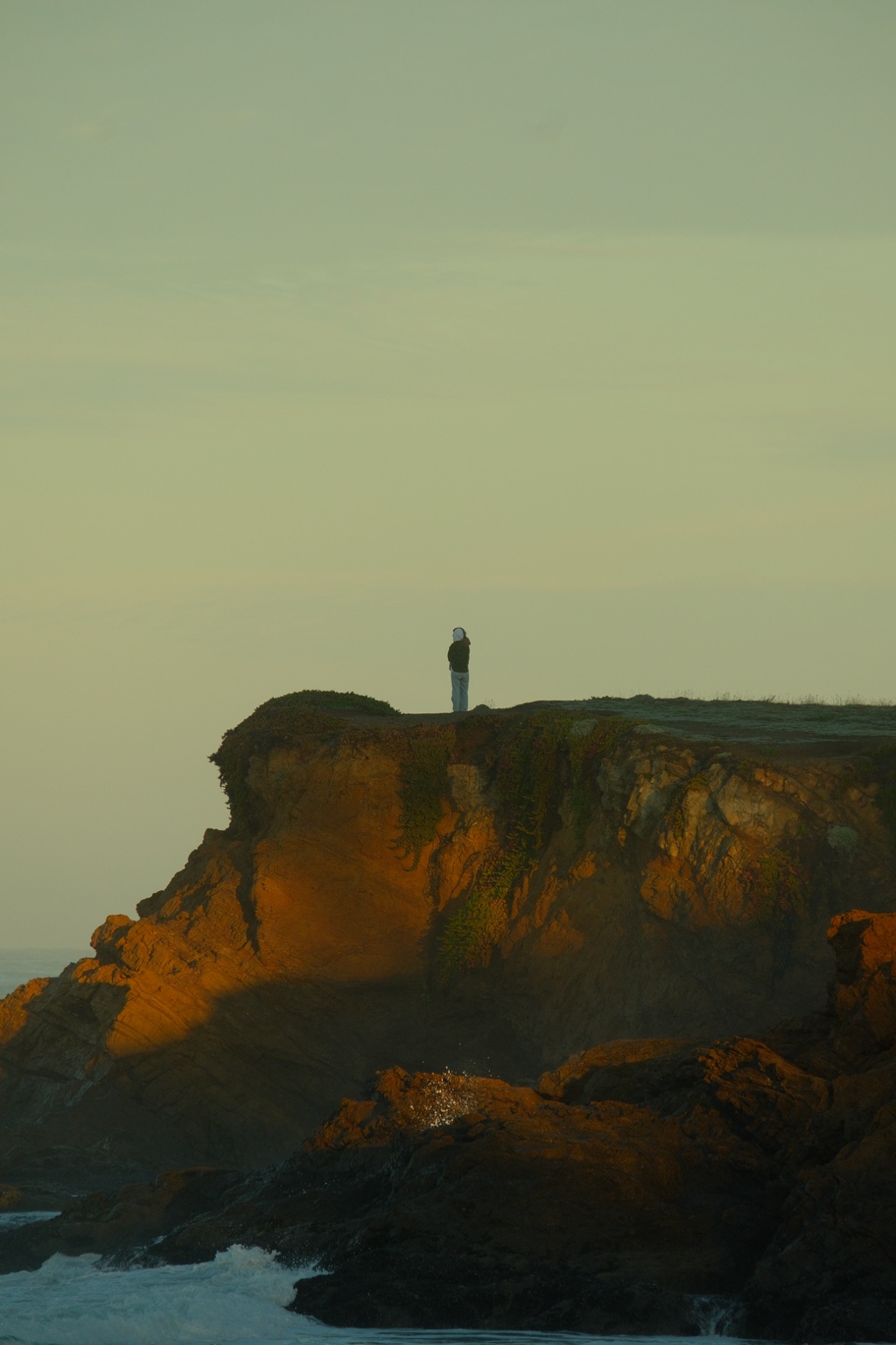 A lone figure stands atop a golden coastal cliff