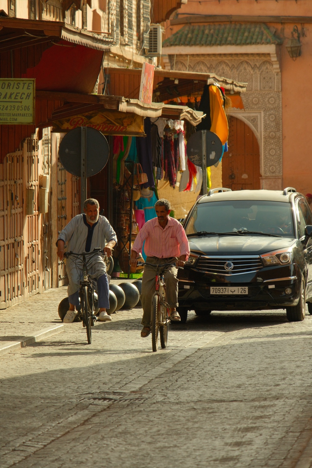 Two cyclists ride along a colorful sunlit street