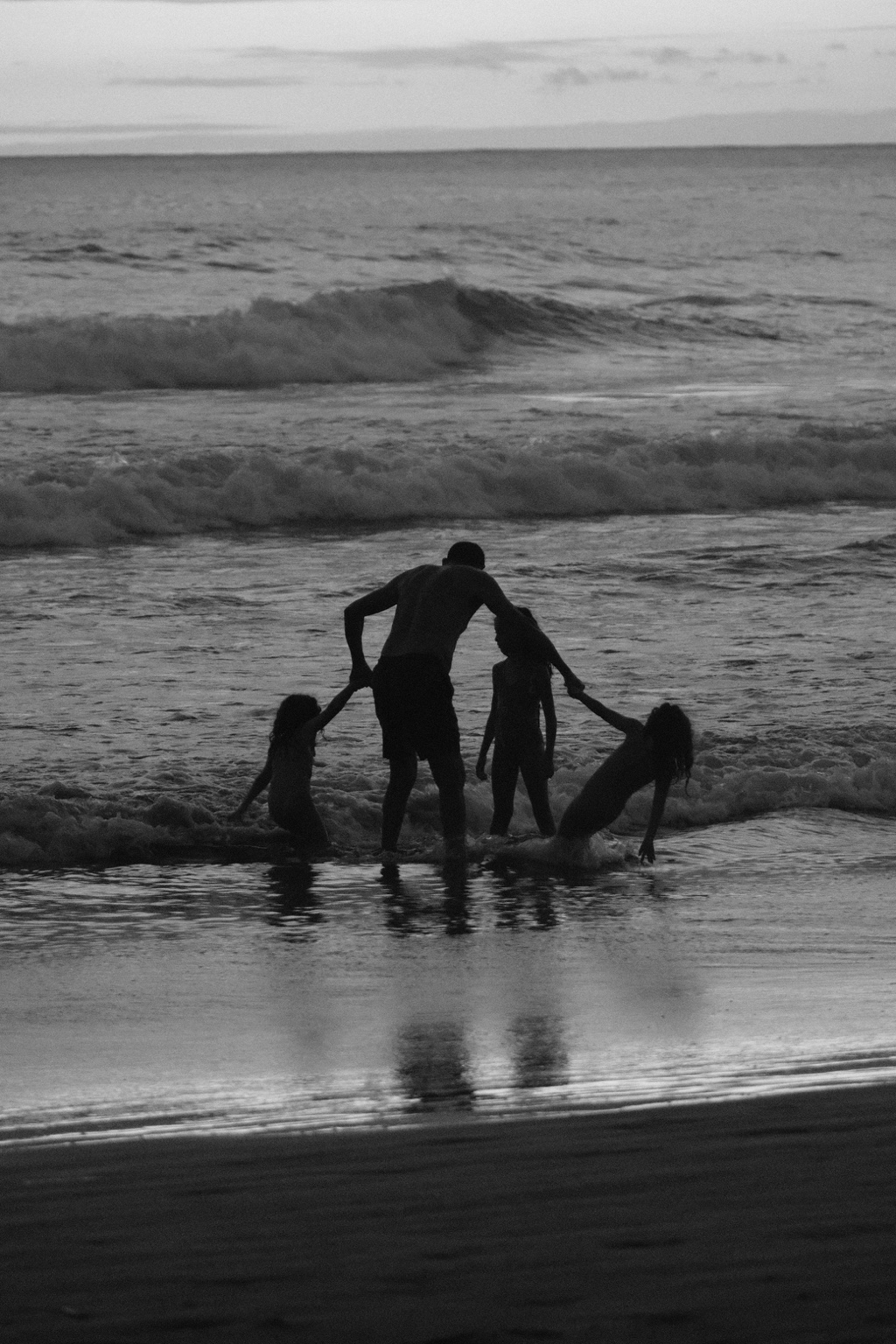 Silhouetted people hold hands at the edge of the surf